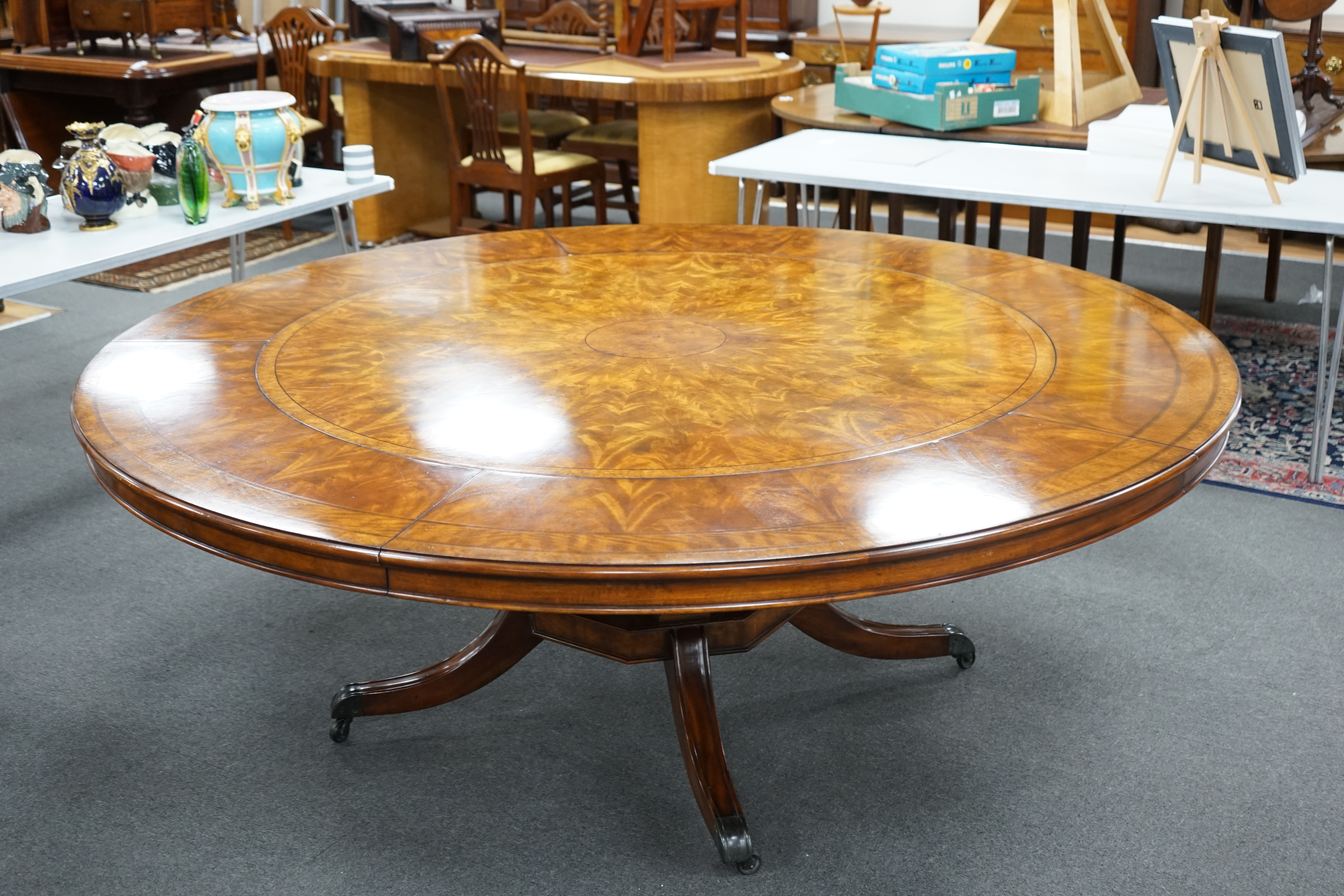 A reproduction George III style circular mahogany extending dining table with detachable segmental outer ring and eight Empire style cherry dining chairs with tan leather seats, table 142cm diameter, 202cm diameter exten